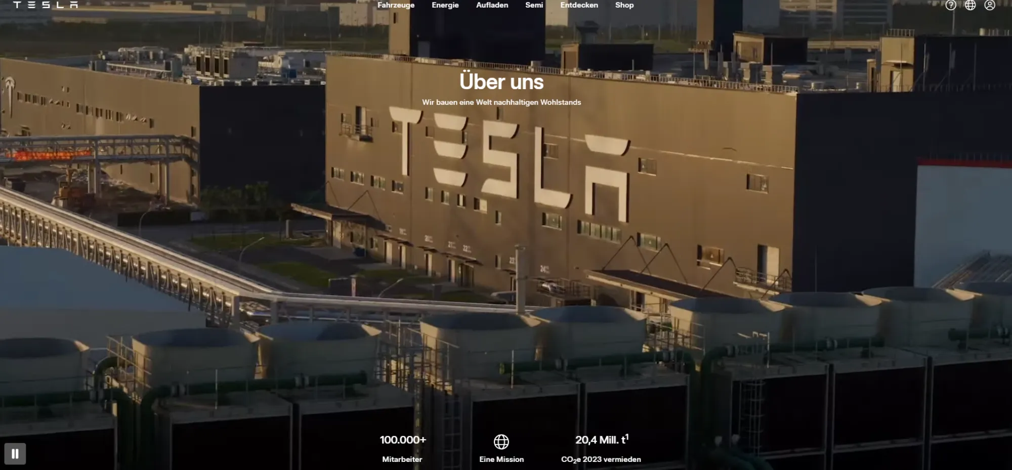 <think> Got it, let's create the alt text. The image shows a large industrial building with "TESLA" prominently displayed on…